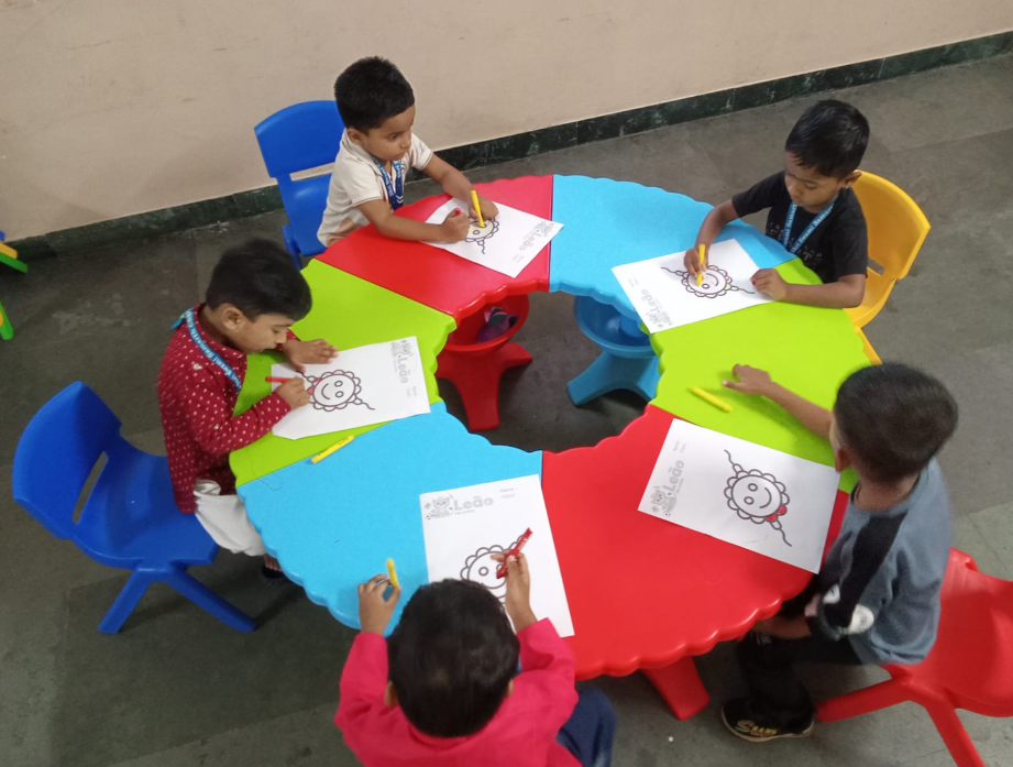 Pre-primary students coloring Rakhi sheets around a flower-shaped table